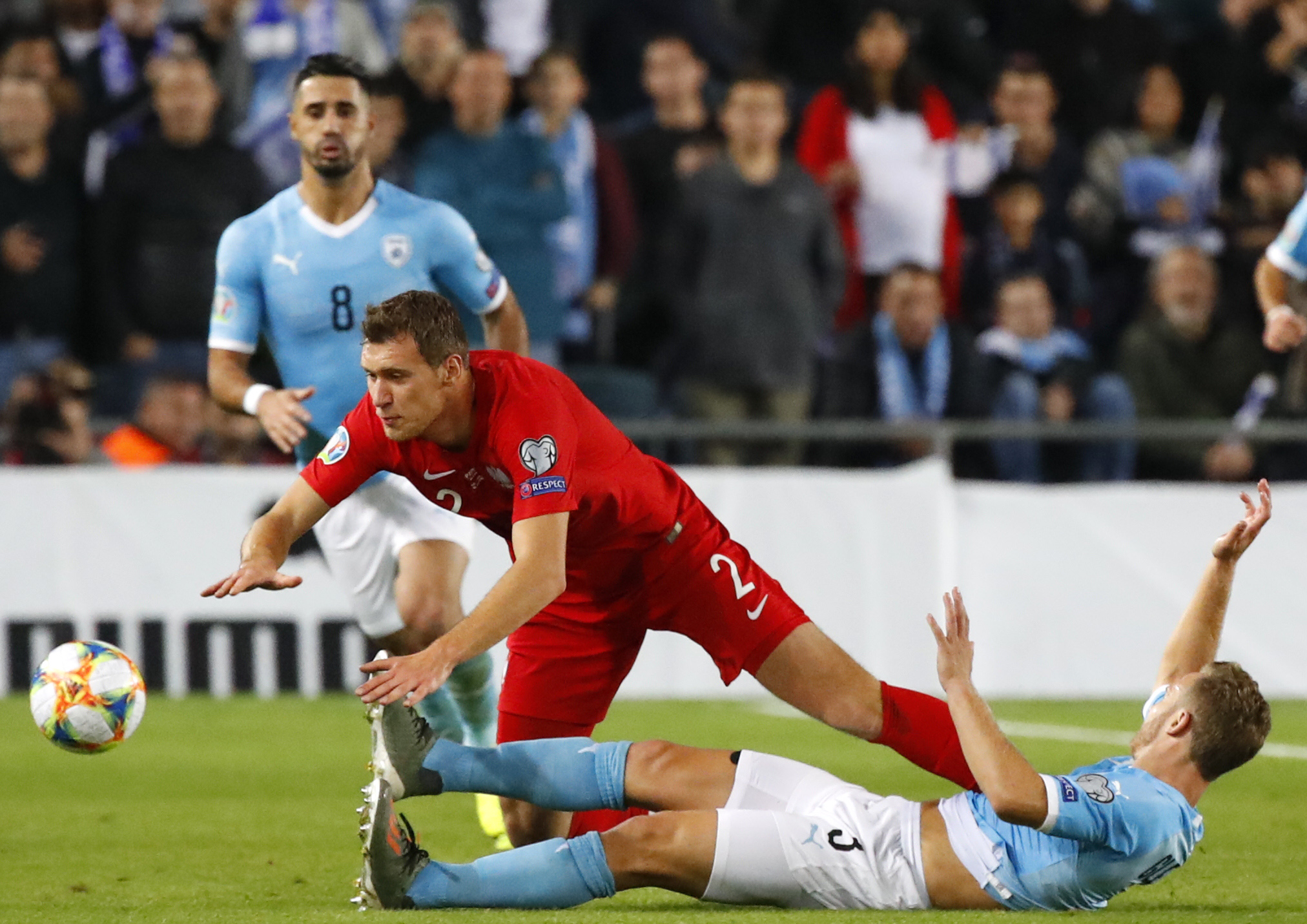 Poland's midfielder Krystian Bielik (C) falls over Israel's midfielder Dan Leon Glazer (bottom) as they vie for the ball during the EURO 2020 group G qualifiers football match between Israel and Poland at the Teddy stadium in Jerusalem on November 16, 2019.