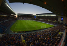 A yellow football in Ibrox stadium decorated with British flags by night
