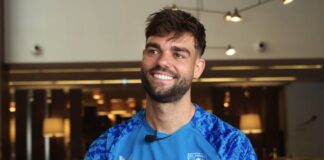 Robin Pröpper smiles during an interview while wearing an FC Twente training top, seated indoors with warm lighting in the background.