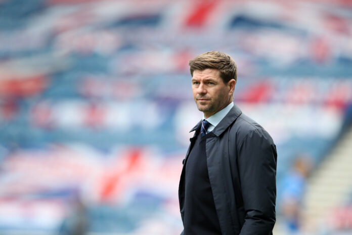 Rangers v Celtic - Ladbrokes Scottish Premiership Steven Gerrard standing on the touchline in a dark coat and tie, with a blurred Union Jack display in the background at Ibrox Stadium.