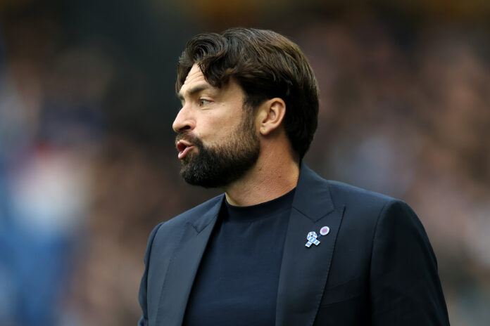 Russell Martin, dressed in a sleek navy blazer and dark top, passionately directs his team from the sideline during the UEFA Champions League qualifier between Rangers and Panathinaikos.