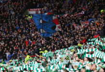 Rangers and Celtic fans in full voice during an Old Firm derby, with Rangers supporters waving a blue bear flag and Celtic fans holding green and white scarves.