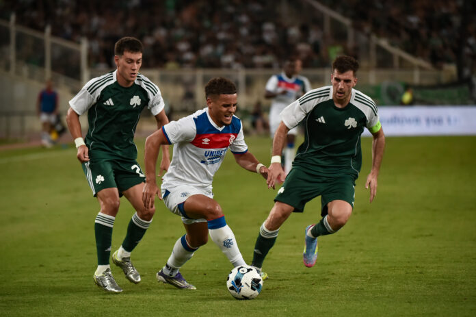 Max Aarons in action for Rangers, dribbling between two Panathinaikos players during a tense Champions League qualifier.