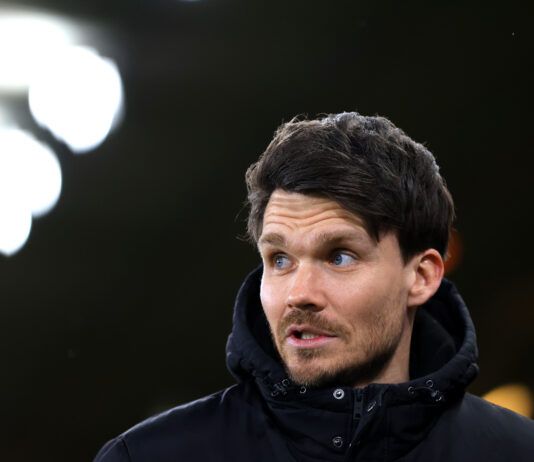 Danny Röhl on the touchline during a Championship match, wearing a black jacket under bright stadium lights
