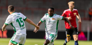 Nigerian winger in green and white kit drives forward with the ball during a pre-season match