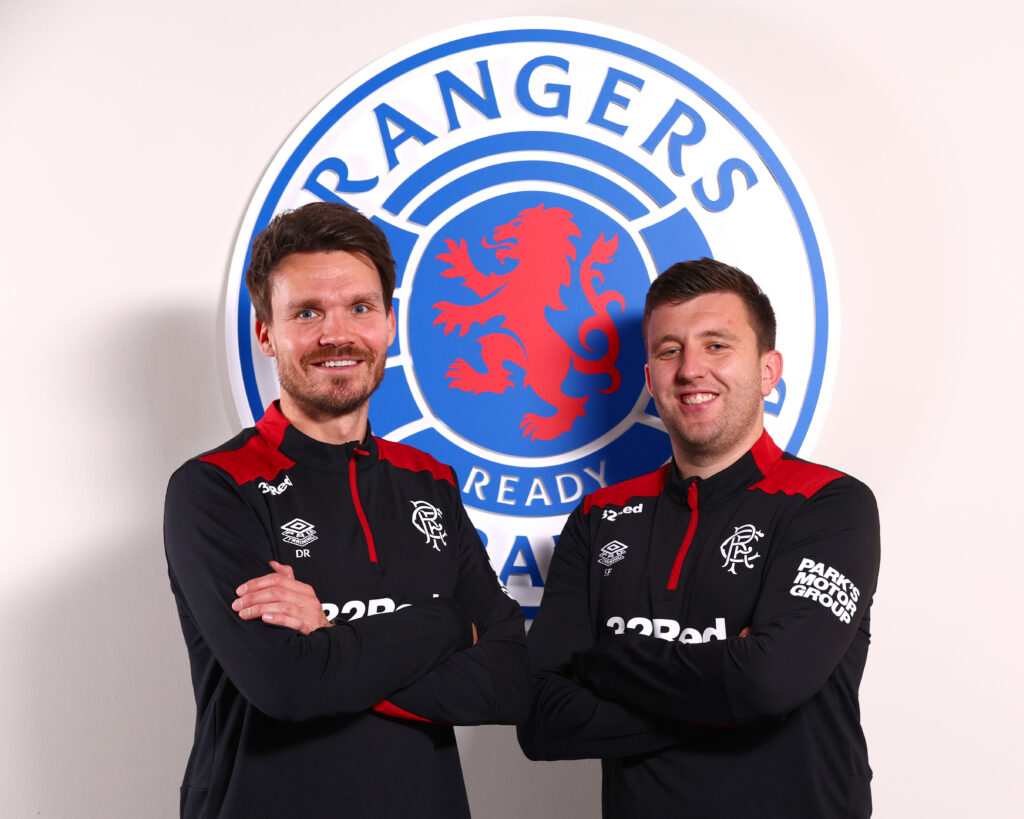 Danny Röhl and Scott Fry standing with arms crossed in front of Rangers badge