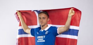 Thelo Aasgaard wearing the Rangers home kit 2026 27 while holding a Norwegian flag during a promotional photoshoot
