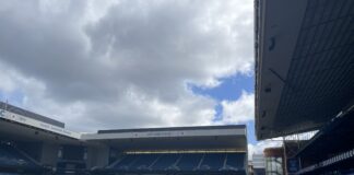 Person using virtual reality equipment on the Ibrox pitch with Rangers FC stands visible in the background