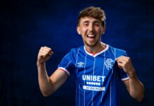 Dan Neil celebrates while wearing the Rangers home shirt after signing for Rangers.